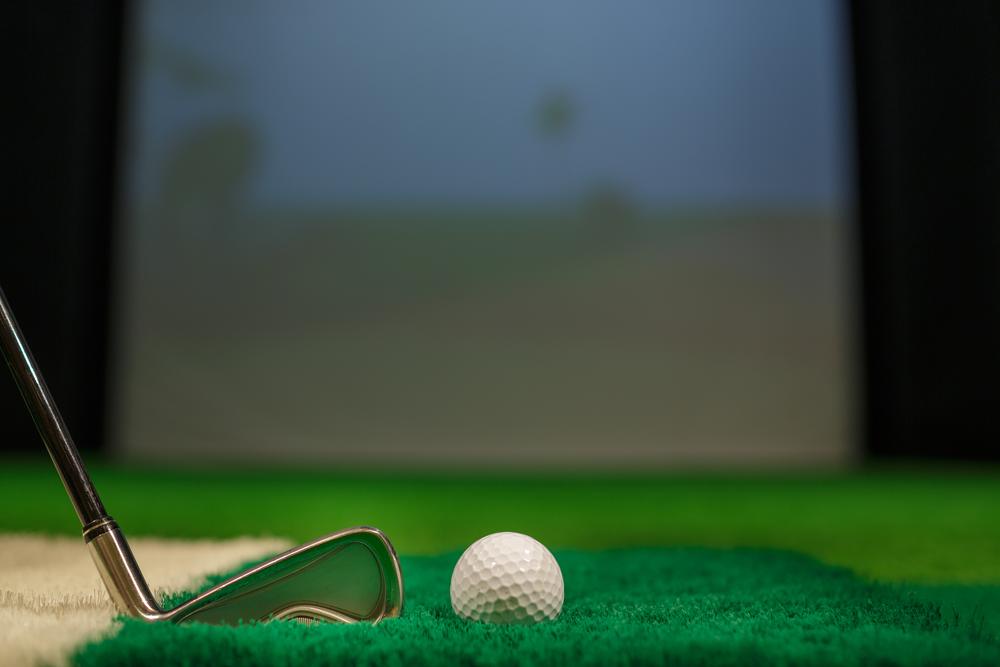 Iron club head beside a golf ball on simulator turf